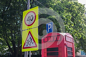 Road signs Caution, children and Speed limit 40 on pole with wires, next to them red booth with inscription in russian COALS, behi