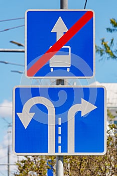 Road signs Direction of motion traffic on the lanes closeup against green trees and blue sky in sunny day