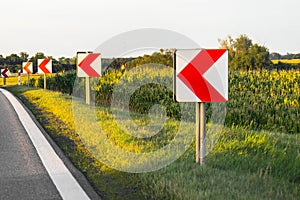 Road signs in European style warn of a sharp turn on a narrow road, a sharp turn