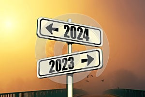 Road signs indicate the path to the new year 2024 and the old year 2023 on a blue sky with fog and sunset, creative idea. Choose a