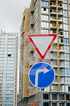 Road signs: main road, pedestrian crossing, stop is prohibited. In the background, the city under construction