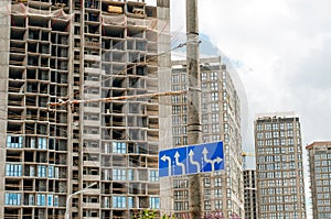 Road signs: main road, pedestrian crossing, stop is prohibited. In the background, the city under construction