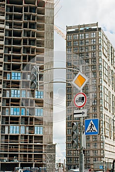 Road signs: main road, pedestrian crossing, stop is prohibited. In the background, the city under construction