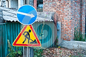 Road signs, traffic sign on the background of a green fence and a brick wall, traffic sign to the right, road works sign
