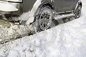 Road snow flies up from a vehicle's spinning wheel. Car's wheels spin and spew up pieces of snow it attempts to