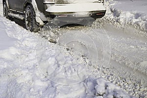 Road snow flies up from a vehicle's spinning wheel. Car's wheels spin and spew up pieces of snow it attempts to