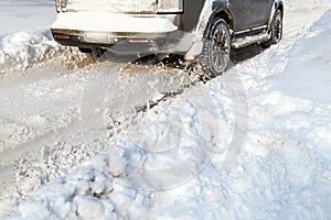 Road snow flies up from a vehicle's spinning wheel. Car's wheels spin and spew up pieces of snow it attempts to gain