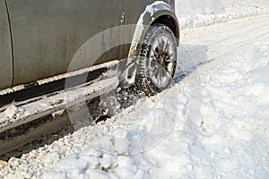 Road snow flies up from a vehicle's spinning wheel. Car's wheels spin and spew up pieces of snow it attempts to gain