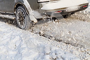 Road snow flies up from a vehicle's spinning wheel. Car's wheels spin and spew up pieces of snow it attempts to gain