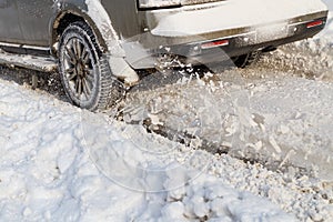 Road snow flies up from a vehicle's spinning wheel. Car's wheels spin and spew up pieces of snow it attempts to gain photo