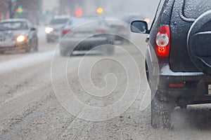 Road snow pieces flow from wheels of dirty car accelerating in daylight city with selective focus