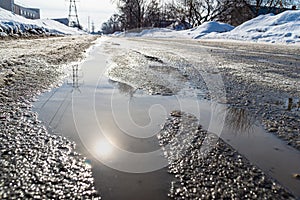 Road with spring streams that flow along the road covered with ice and dense snow, reflection of sun, selective focus