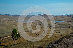 Road in steppe with lakes among hills and mountains covered with green grass. Baikal nature