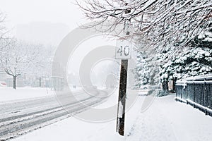 Road street speed sign under snow. Heavy snowfall and snowstorm in Toronto, Ontario, Canada. Snow blizzard and bad weather winter