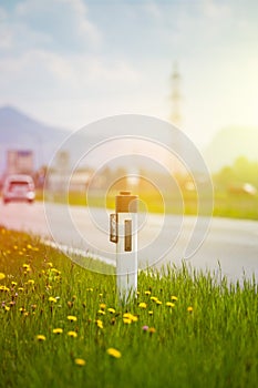 Road in the summer: reflector post, cars, flowers and green grass. Sunbeam