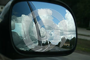 The road, sunny summer sky with clouds and trees reflection in car side mirror