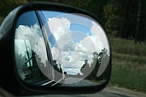 The road, sunny summer sky with clouds and trees reflection in car side mirror