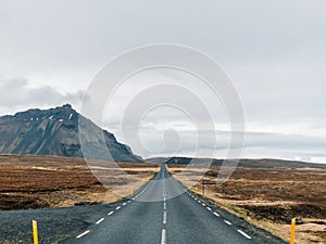 Road surrounded by hills covered in greenery and snow under a cloudy sky in Iceland photo
