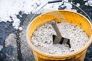 Road or thawing salt into a yellow bucket, icy ground