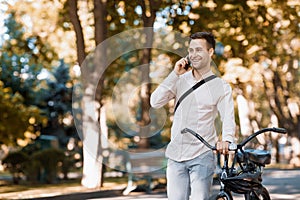 Road to work on eco transport. Guy walks with phone in park with bike