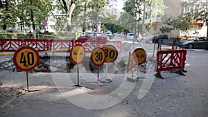 Road traffic warning signs and a plastic fence around a big hole in the asphalt from where steam comes out