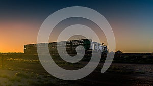 A road train runs along the Stuart highway at sunset