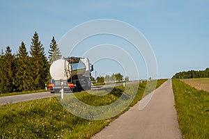Rear view of white truck with chrome tanker driving on the asphalt road in rural landscape