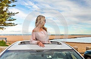 Road trip summer beach vibes.  Carefree woman in sunroof car by beach