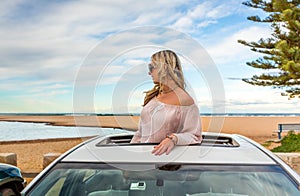 Road trip to beach. Carefree woman in sunroof with views