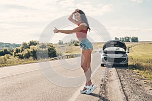 Road trip, transport, travel, gesture and people concept - happy young women with broken car showing hitchhiking gesture