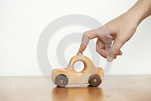 Road trip and travel concept. Hand playing with natural wooden car toy on table on white wall background. Space for text. Eco