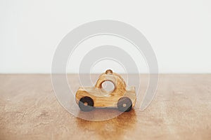 Road trip and travel concept. Stylish natural wooden car toy on table on white wall background. Space for text. Eco friendly