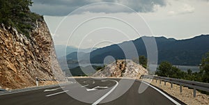 The road turns a mountain. Pointers on the pavement. Mountains, lake and clouds in the background