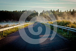 Road between two lakes in the misty sunris