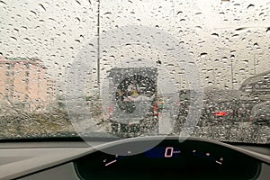 Road view through front car window mirror with rain drops.