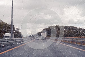 Road view through windshield car window with going rain drops during driving at speed. Unfocused highway. Autumn.