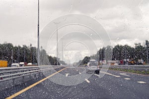 Road view through windshield car window with going rain drops during driving at speed. Unfocused highway. Autumn.