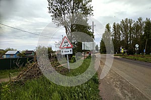 The road in the village before the rain. Traffic sign `Slippery road`.