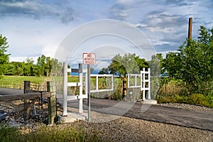 Road with white gate and sign post against trees and grassy field on a sunny day