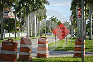 Road work ahead sign and barrier cones on street site as warning to cars about construction and utility works