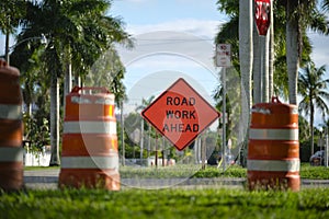 Road work ahead sign and barrier cones on street site as warning to cars about construction and utility works