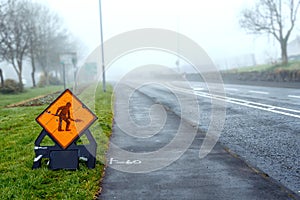 Road work sign in focus. Asphalt road in town in fog. Dangerous conditions concept. Mist covers street. Nobody. Mysterious mood.