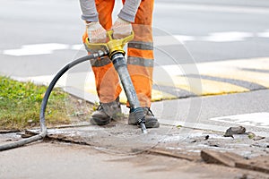 Road worker breaking asphalt pavement with pneumatic construction hammer