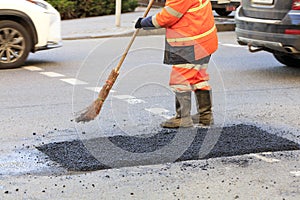 A road worker collects fresh asphalt with a panicle on the part of the road being repaired