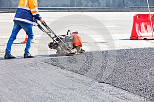A road worker compacts asphalt with a gasoline vibratory compactor