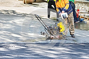 A road worker fills up a compactor tank to repair a road section by compacting fresh asphalt. Copy space