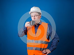 Road worker. A guy in a construction helmet and an orange vest is drinking coffee