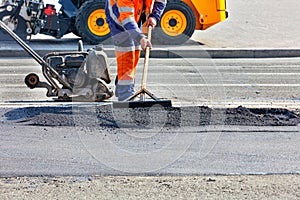 A road worker is leveling fresh asphalt on a road section against a background of road equipment