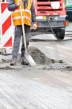 A road worker in an orange vest on the background of a working area for road repair