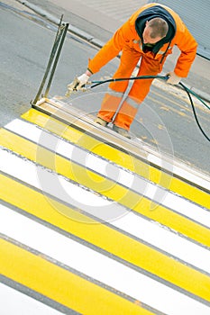 Road worker painting and remarking pedestrian crossing lines on asphalt surface